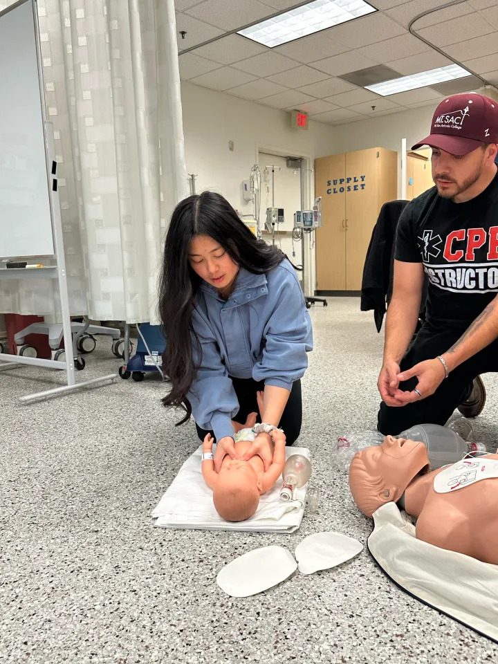 Student practicing infant CPR on a training manikin while the instructor watches